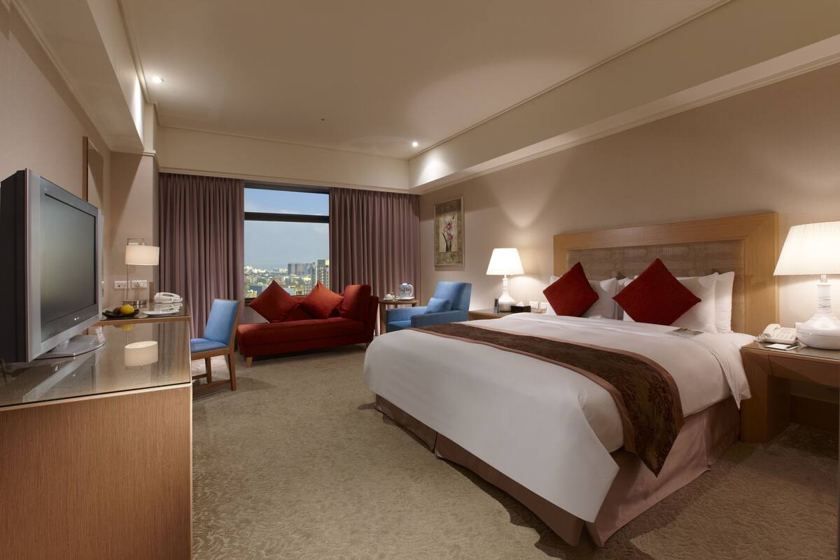 Een hotelkamer met een groot bed, een televisie, een bureau, een stoel en uitzicht op de stad.