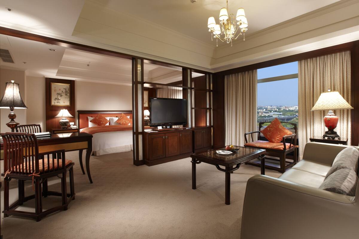 Een hotelkamer met een bed, een televisie, een bank, een bijzettafeltje en uitzicht op de stad.