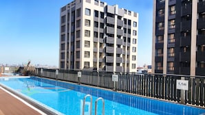 A rooftop swimming pool with a wooden deck, surrounded by modern apartment buildings.
