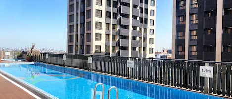 Una piscina en la azotea con un deck de madera, rodeada de modernos edificios de apartamentos.