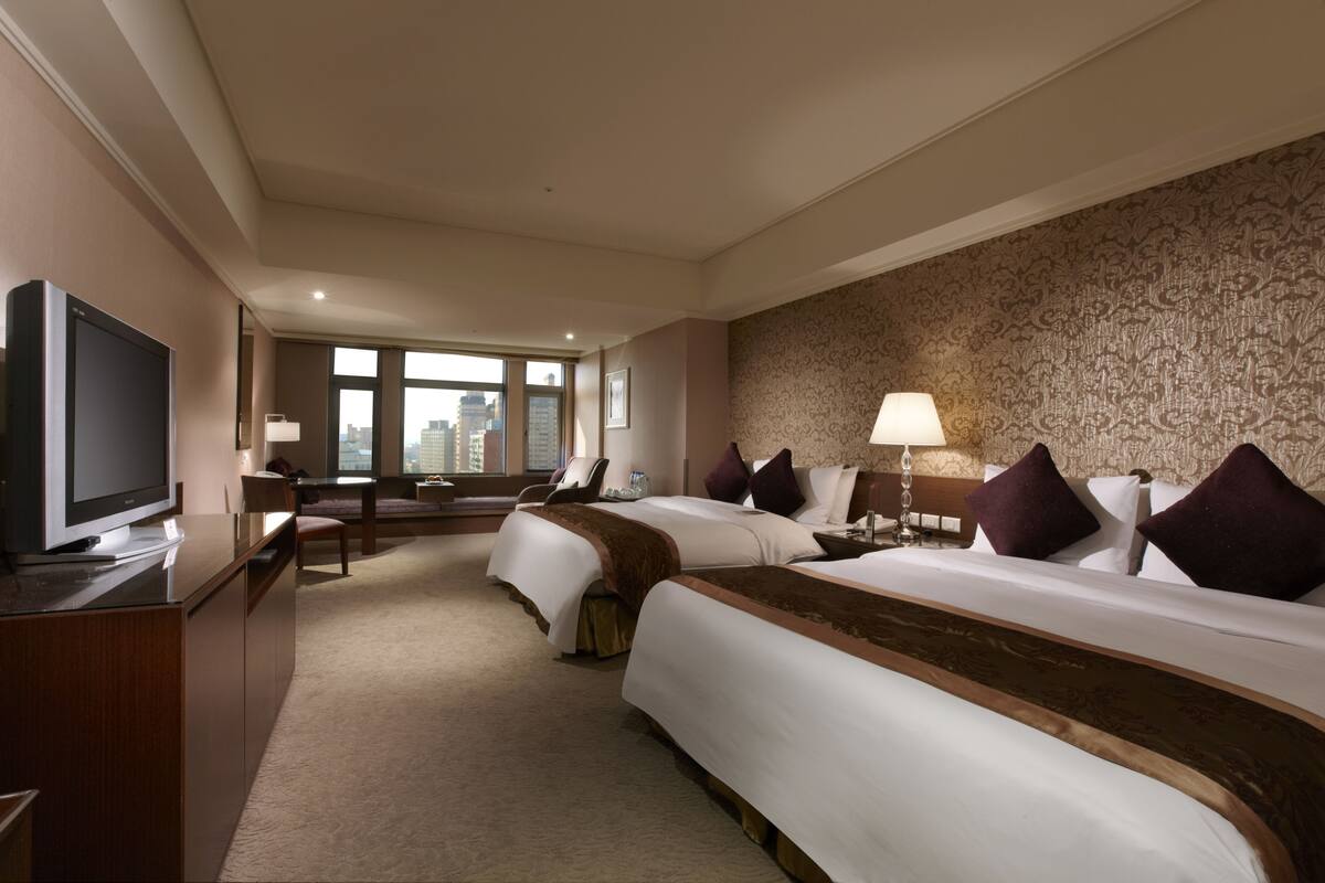 Een hotelkamer met twee bedden, een televisie, een bureau en een groot raam met uitzicht op de stad.