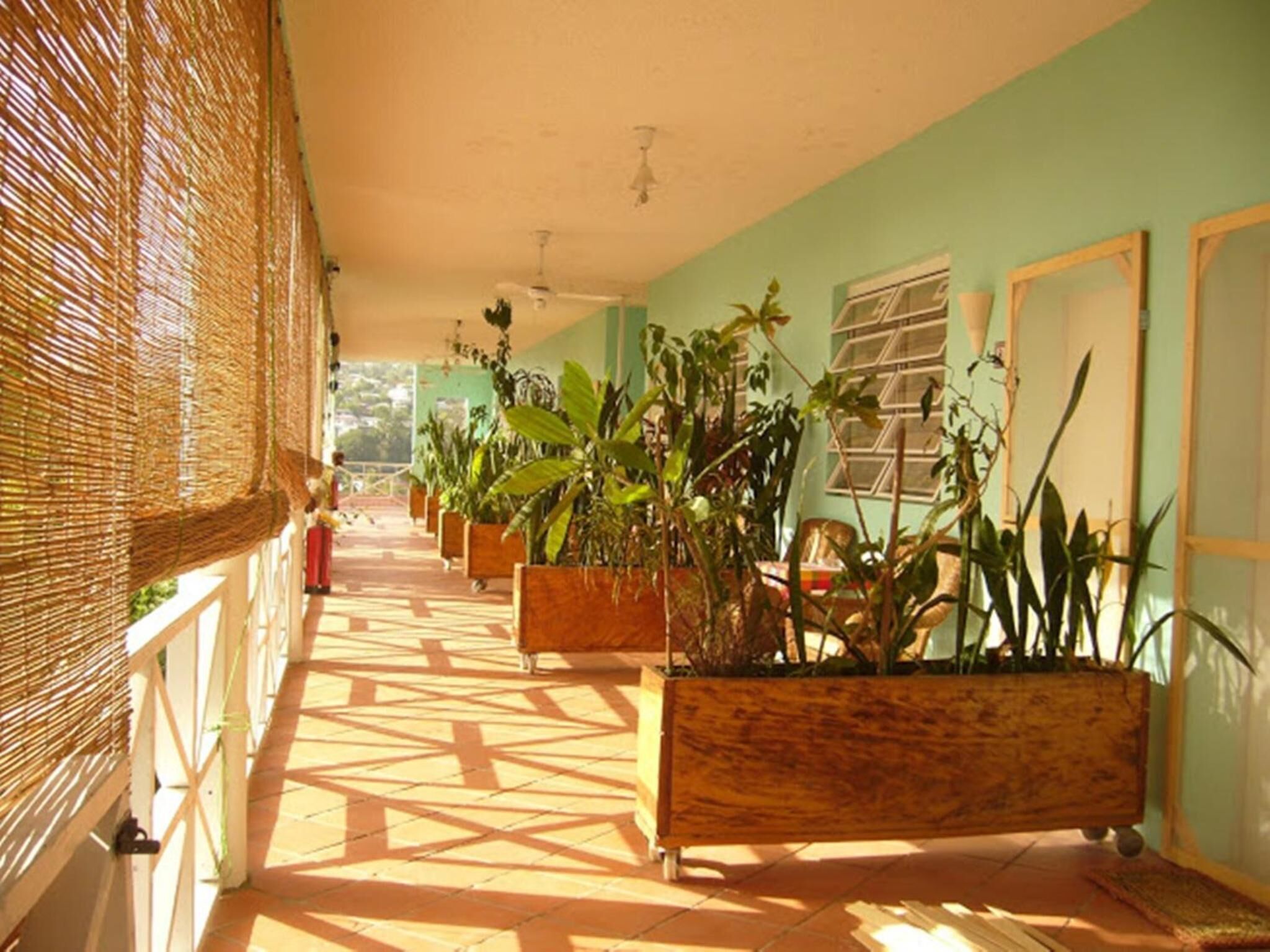 A corridor with tiled flooring, wicker blinds, and wooden planters with various plants.