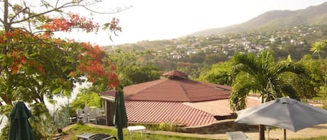 A residential area with a house featuring a red-tiled roof, a swimming pool, and a view of a hillside town.