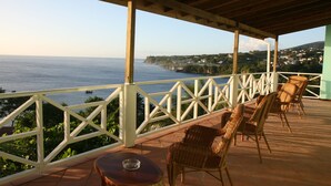 A covered outdoor seating area with wicker chairs and a table, overlooking a coastal view with houses and greenery. - Tamarind Tree Hotel and Restaurant (Salisbury)