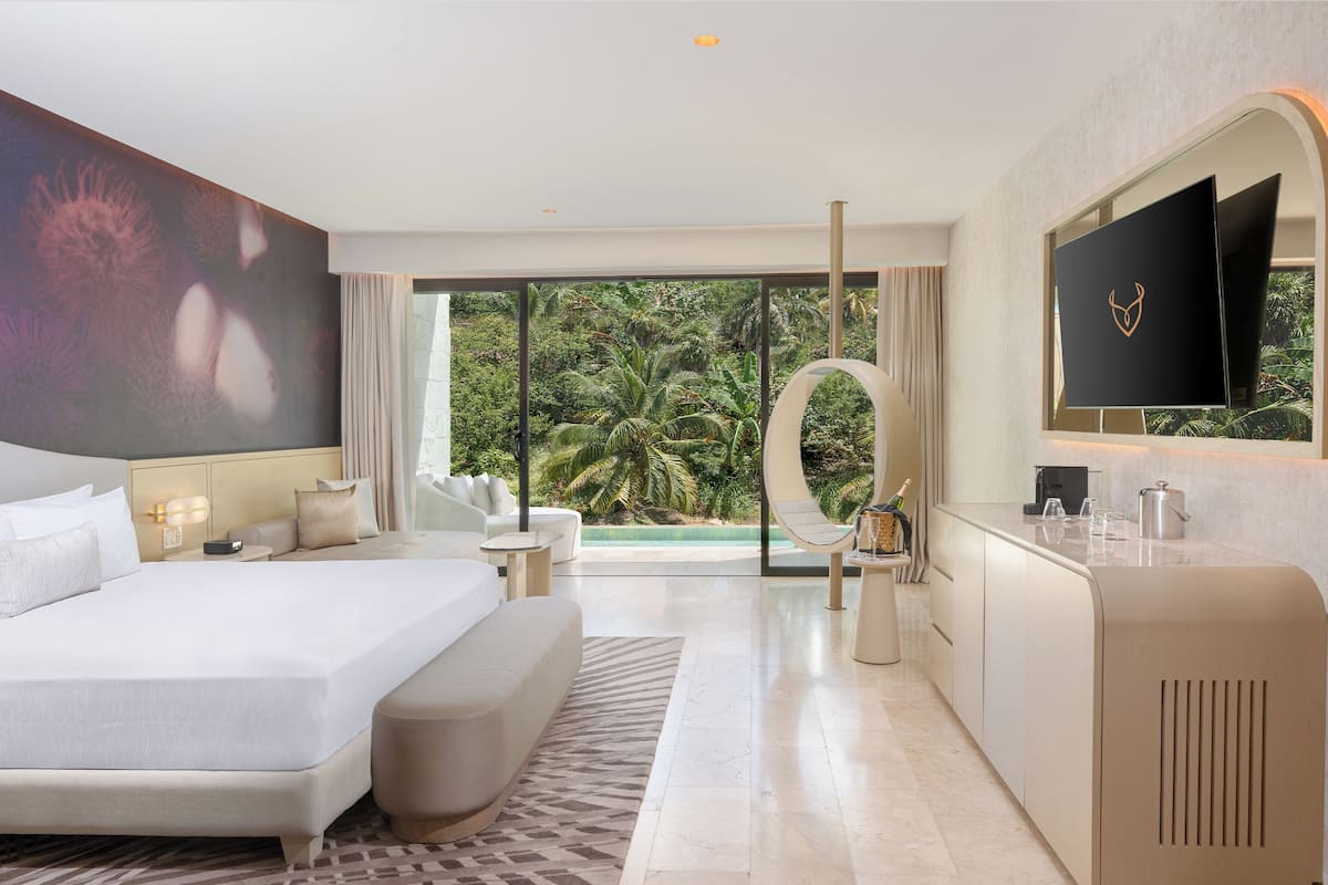 A modern hotel room with a large bed, a seating area, a TV, and a view of the outdoors.