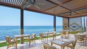 An outdoor seating area with tables and chairs, overlooking a body of water. - Desire Riviera Maya Resort – All Inclusive, Exclusively for Couples (Puerto Morelos)
