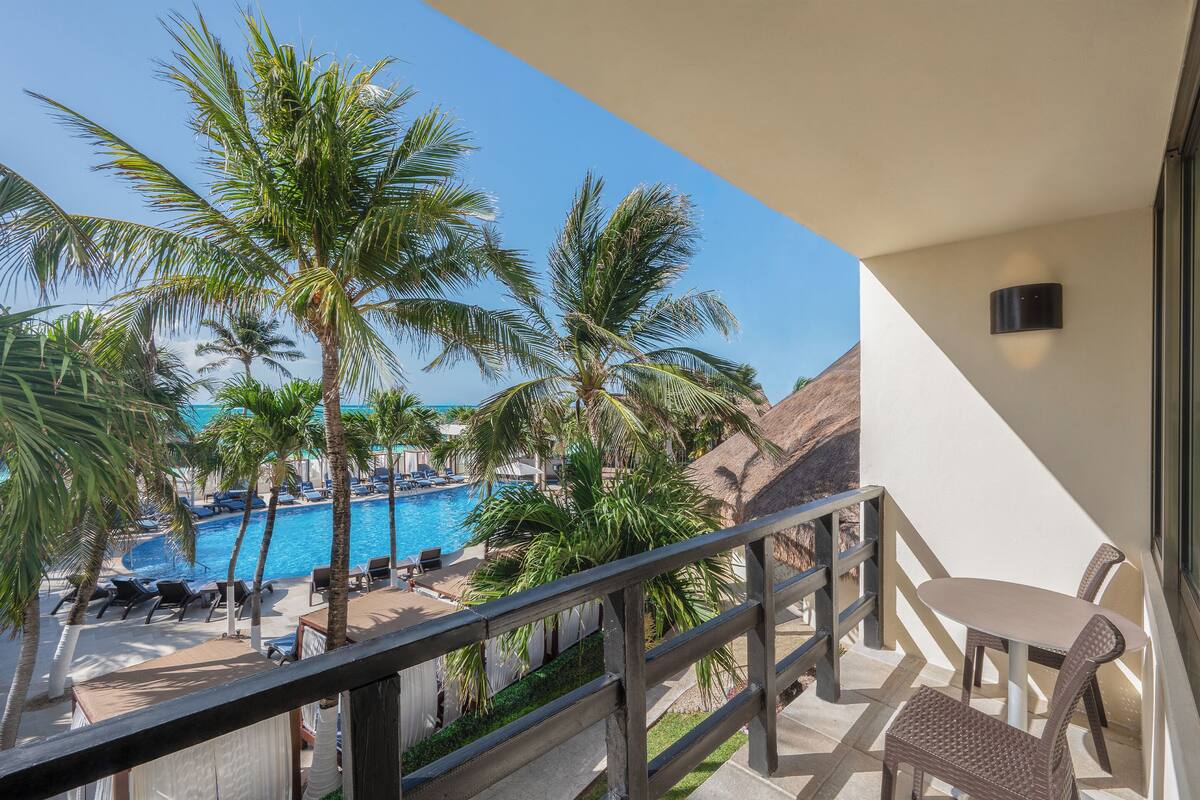 A balcony with a view of a swimming pool, palm trees, and lounge chairs.