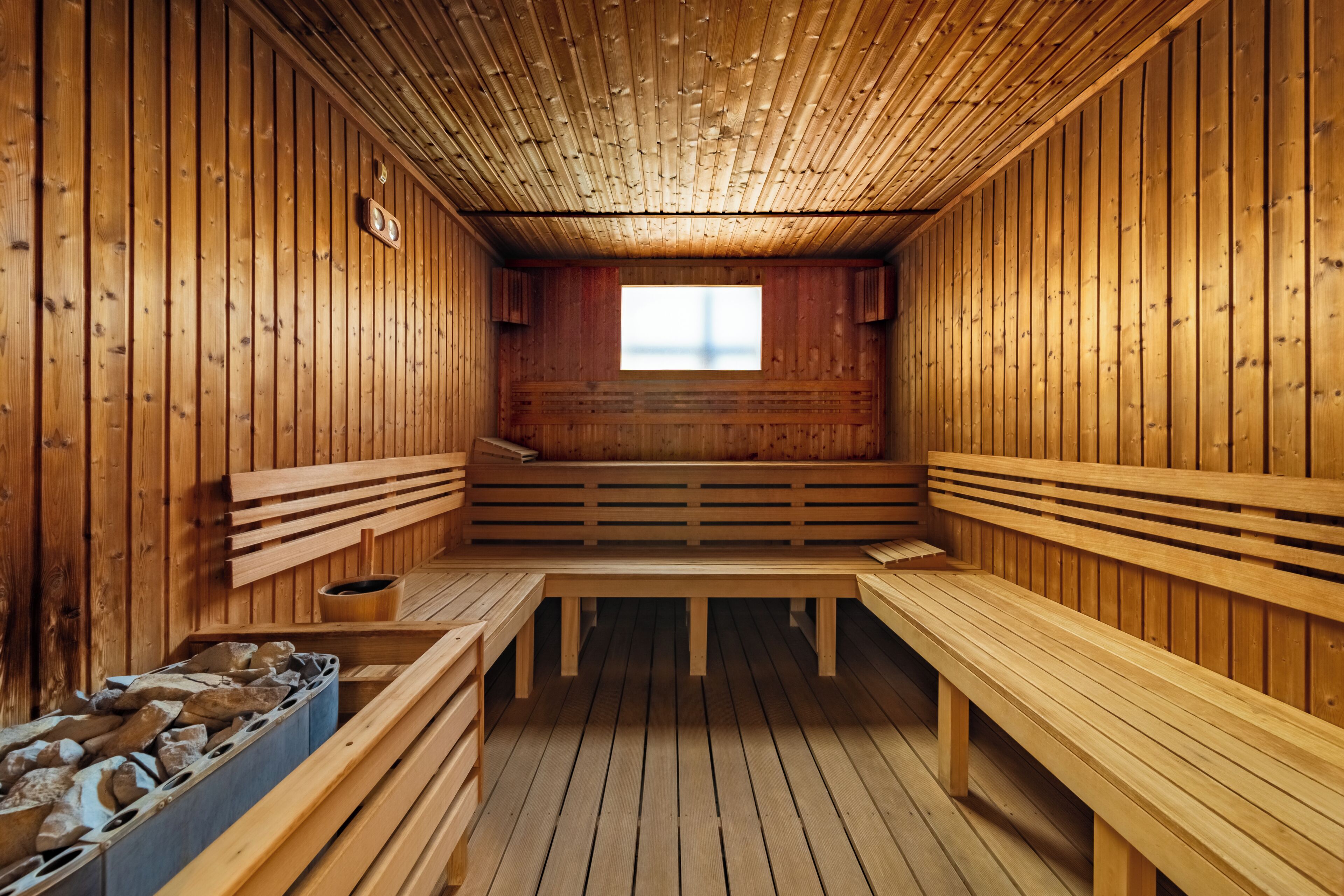 Een sauna met houten banken en een middenbank, een raam en een houten plafond.