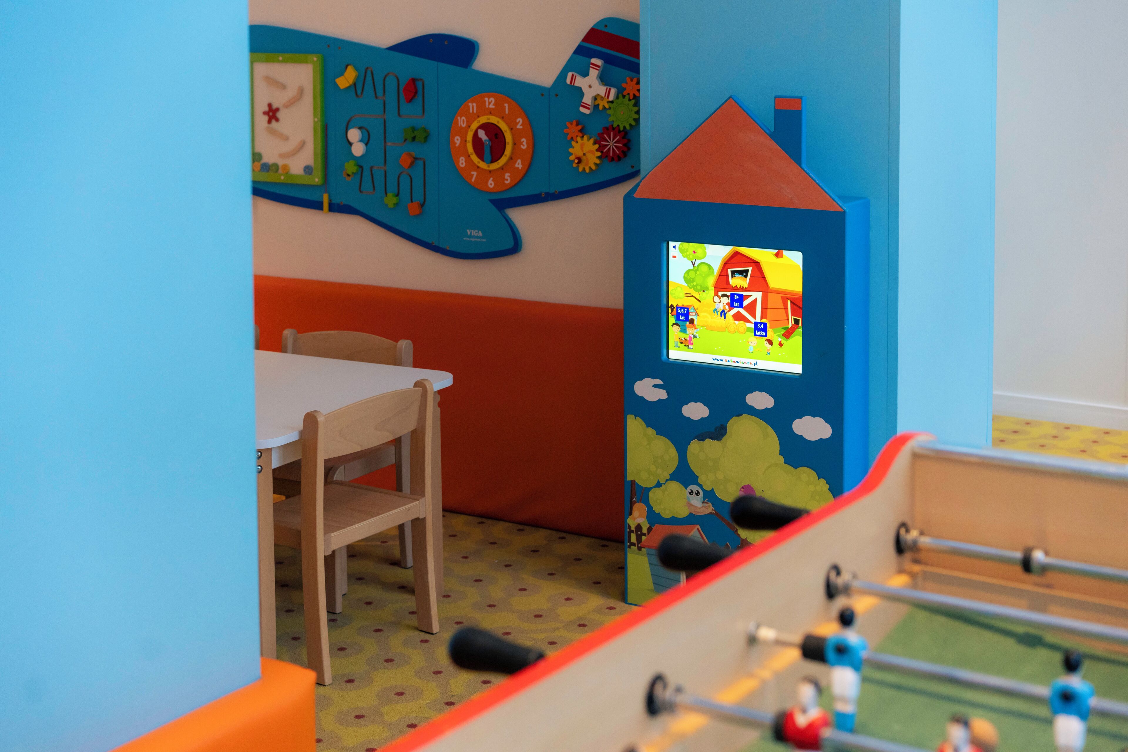 A children's play area with a foosball table, a wooden chair, and a wall with educational decorations.