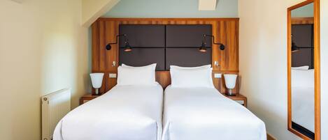 Una cama doble con cabecera de madera, dos mesitas de noche con lámparas y un espejo grande en la pared.