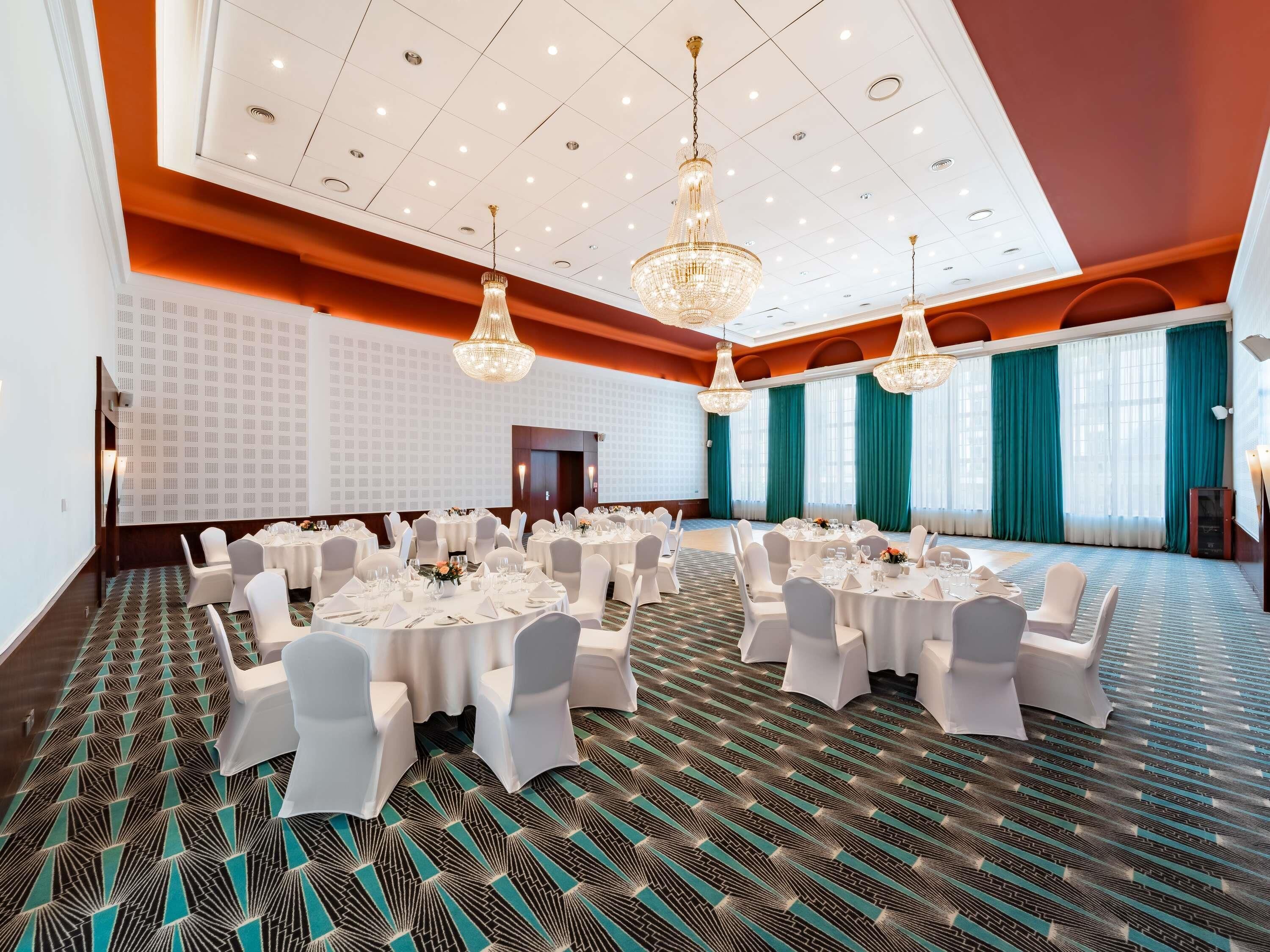 Un salón de conferencias con mesas redondas, sillas blancas y candelabros.