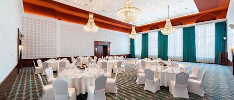 Une salle de conférence avec des tables rondes, des chaises blanches et des lustres.