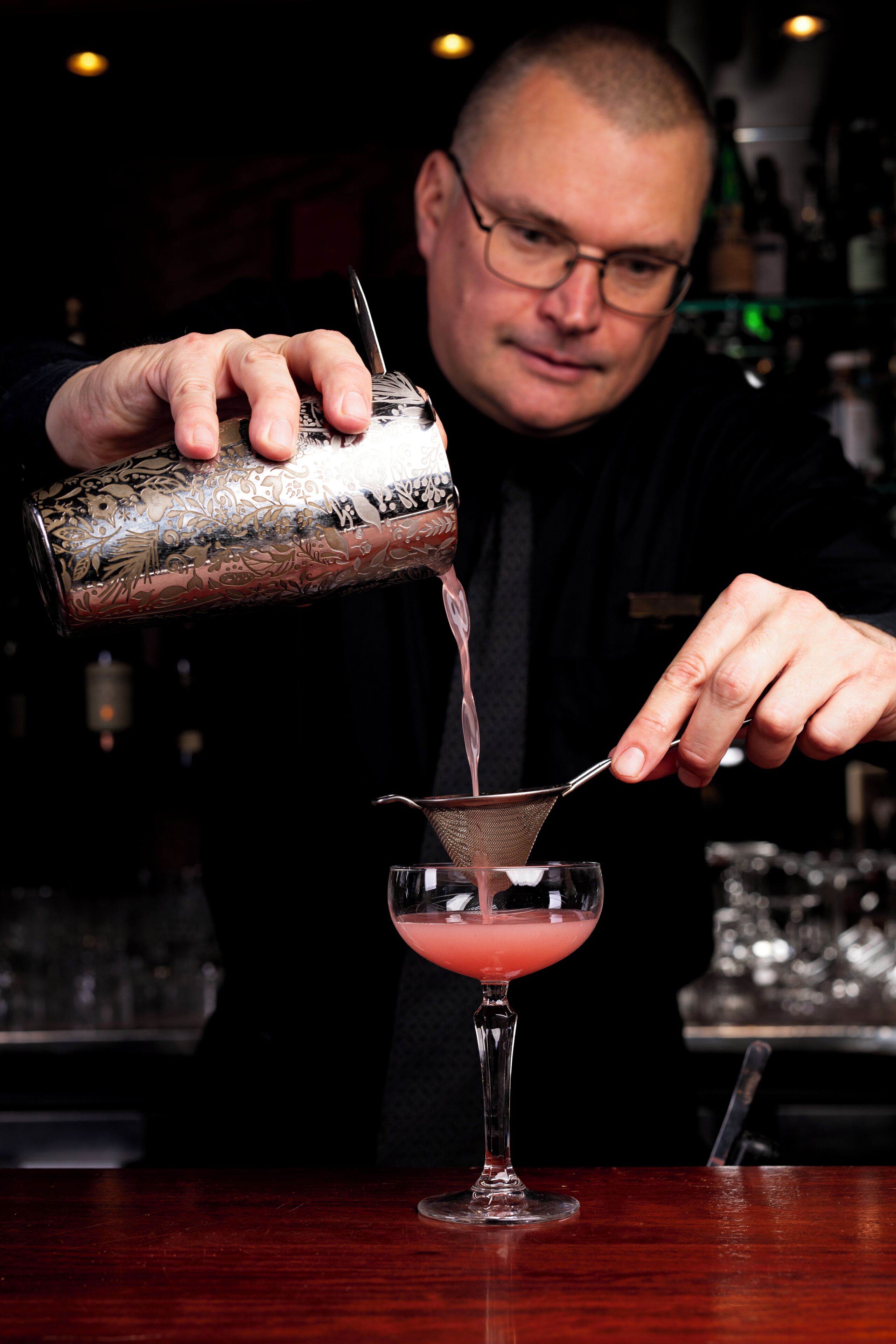 A person pouring a pink liquid into a martini glass.