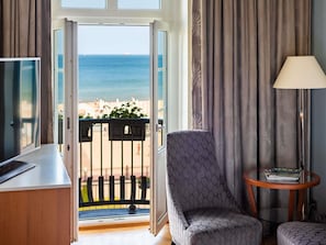 A room with a view of the sea, a chair, a table with a lamp, and a door leading outside.