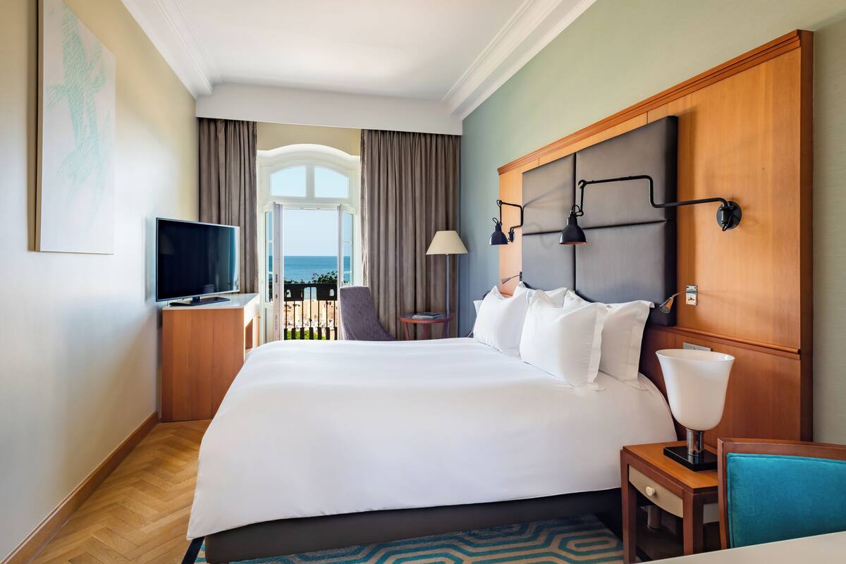 Hotellihuone, jossa on suuri sänky, televisio, lamppu, pieni pöytä ja näkymä ulos.