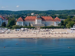 A hotel with a large building, a beach with umbrellas, and a waterfront. - Sofitel Grand Sopot (Sopot)