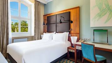 A hotel room with a large bed, a desk, a chair, a window with curtains, and a wall-mounted TV.