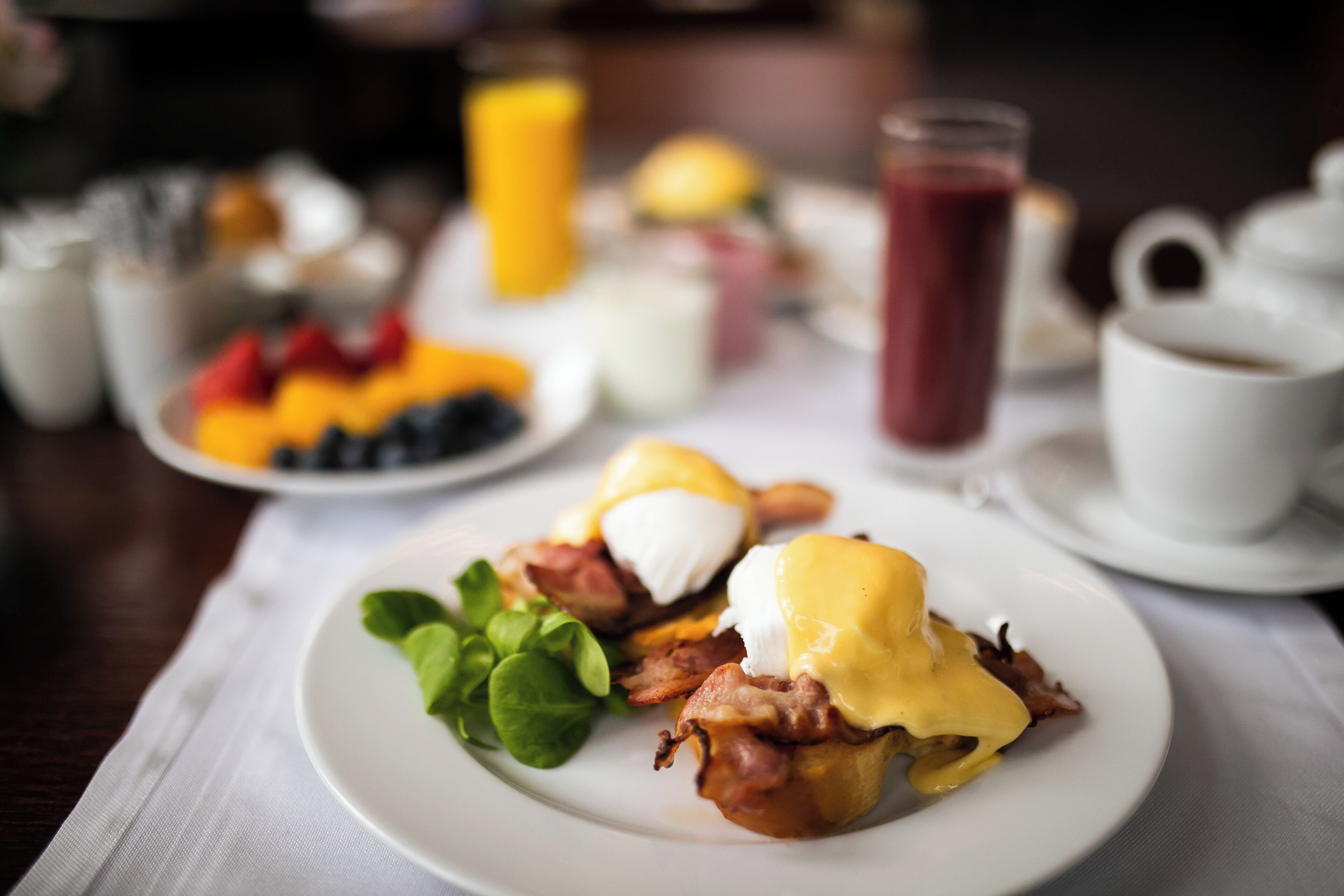 Una mesa con desayuno que incluye huevos Benedict, fruta fresca y bebidas.