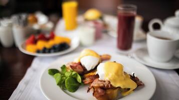Una mesa con desayuno que incluye huevos Benedict, fruta fresca y bebidas.