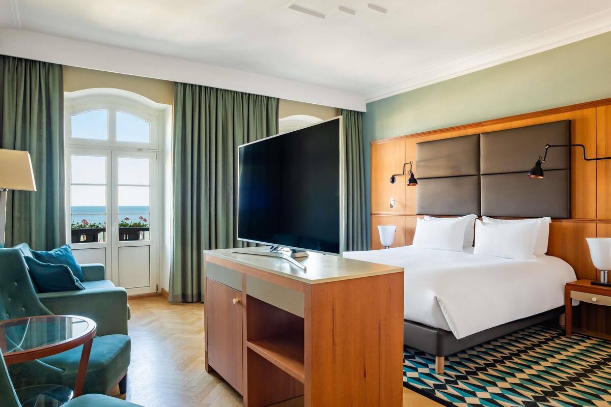 Hotellihuone, jossa on sänky, työpöytä, televisio, tuoli ja näkymä merelle.