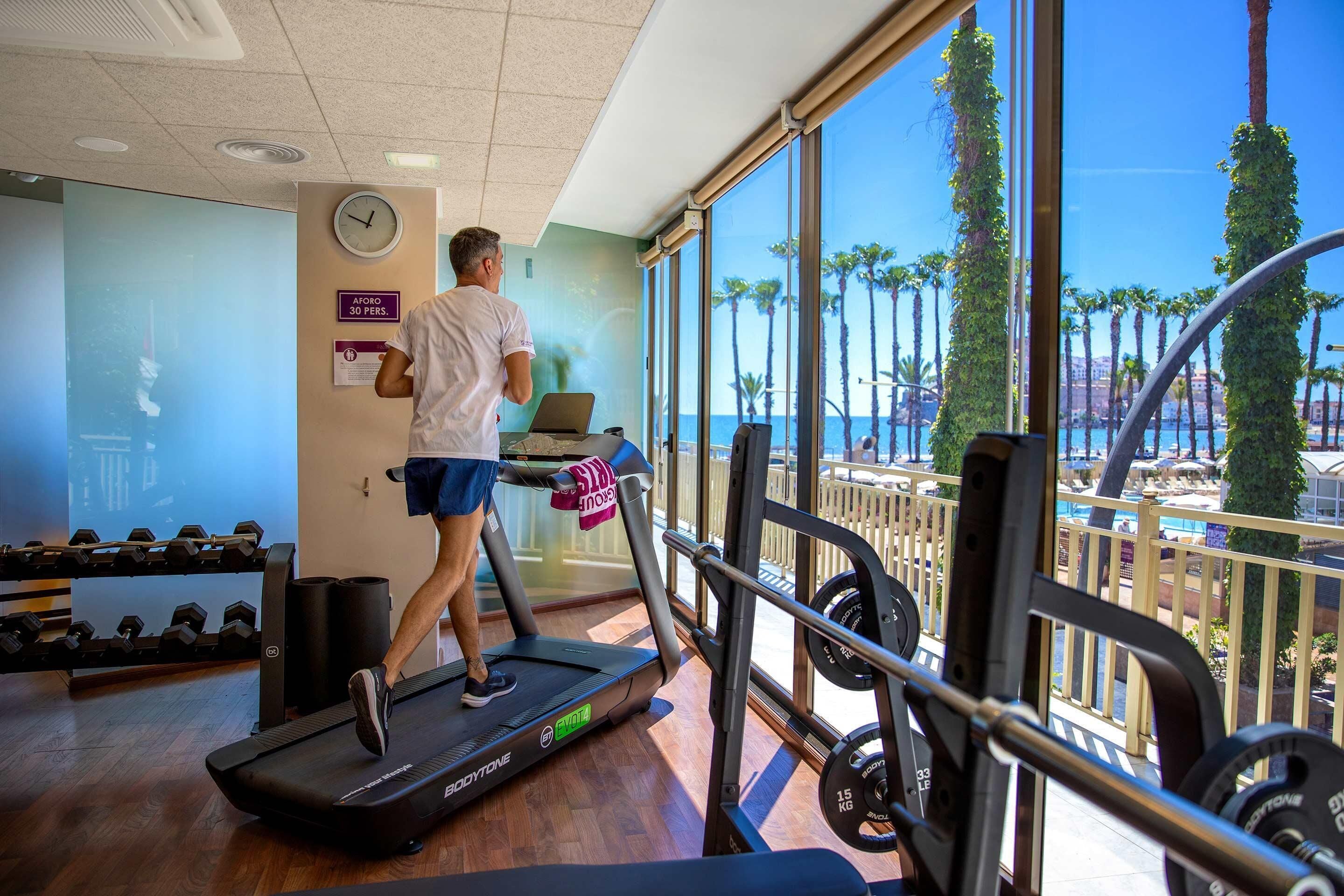 A gym with treadmills, weights, and a large window offering a view of palm trees and a pool.