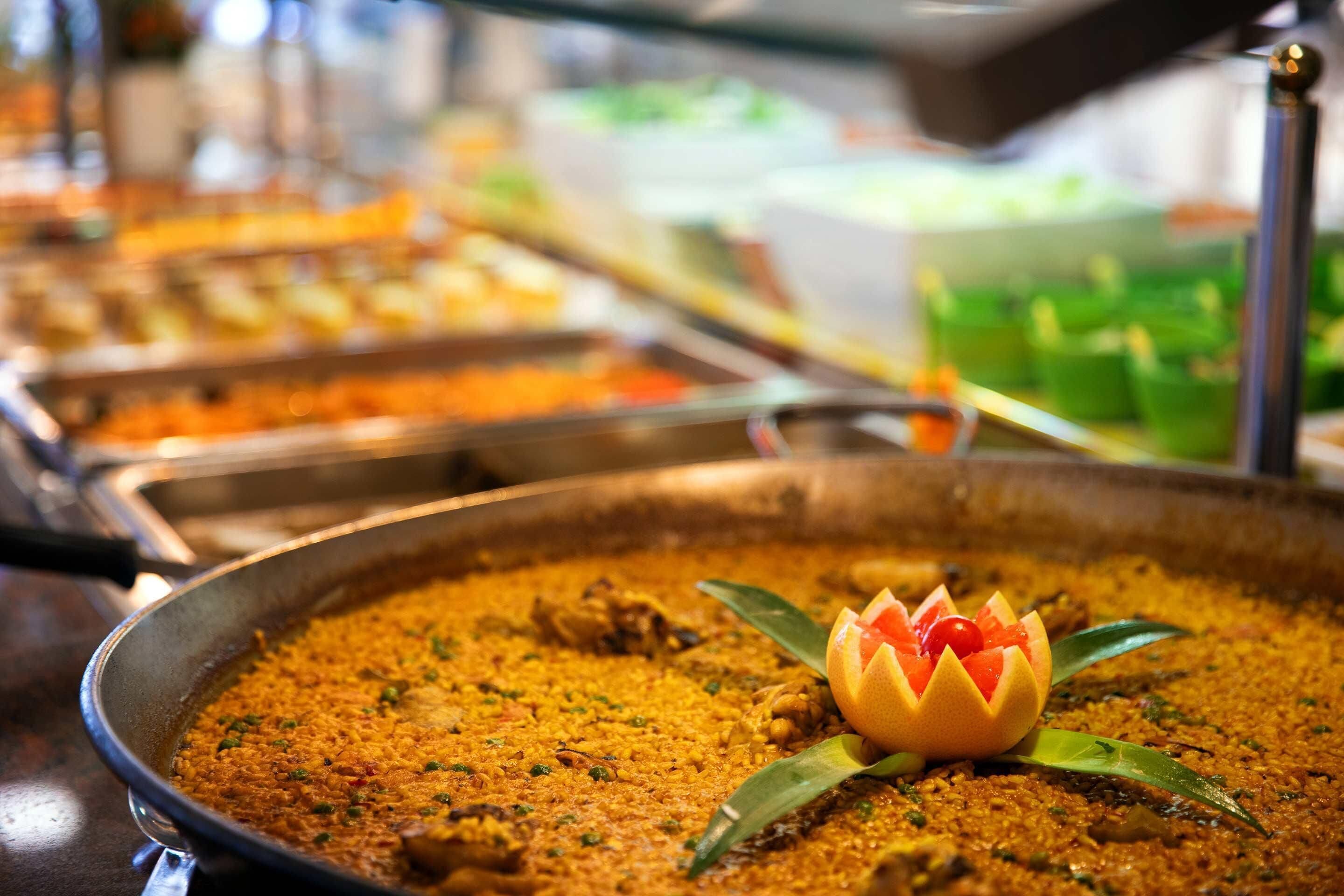 A buffet with a large serving dish of rice and meat, garnished with a flower and green leaves.