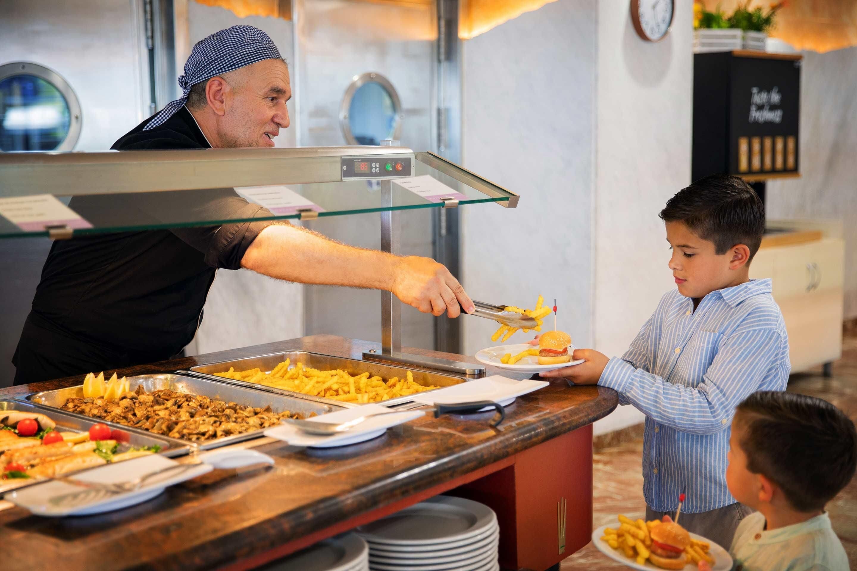 A buffet counter with various food items and a person serving food to a child.