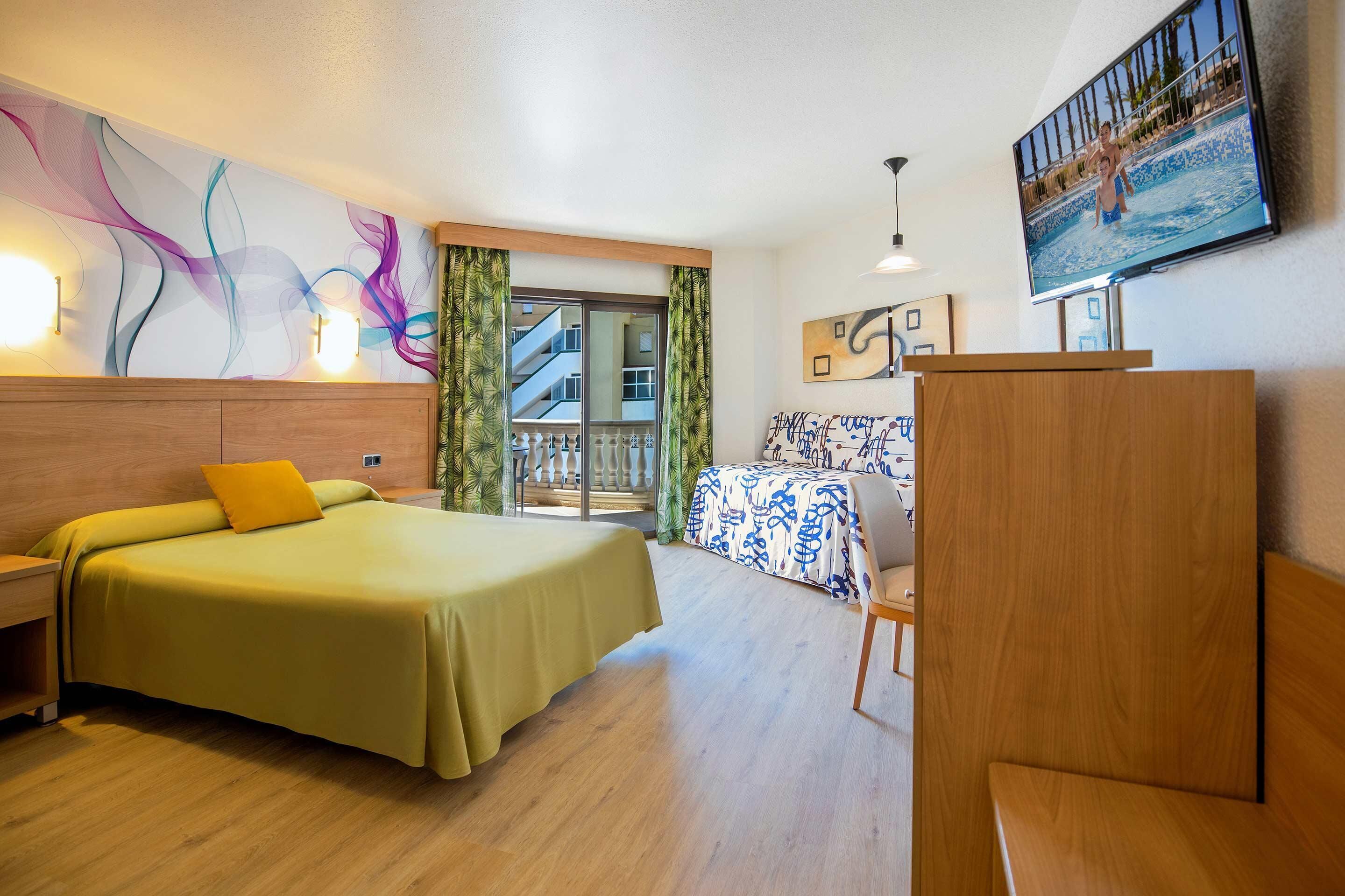 A hotel room with a bed, a desk, a chair, a TV, and a balcony with a view.
