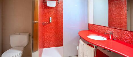 A bathroom with a white toilet, a red-tiled shower area, and a red sink with a mirror.
