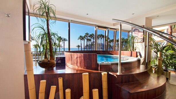 A modern indoor pool area with a view of the ocean, surrounded by bamboo plants and wooden architecture.