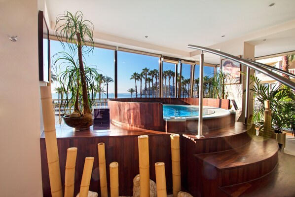 Un área de piscina interior moderna con vistas al océano, rodeada de plantas de bambú y arquitectura de madera.