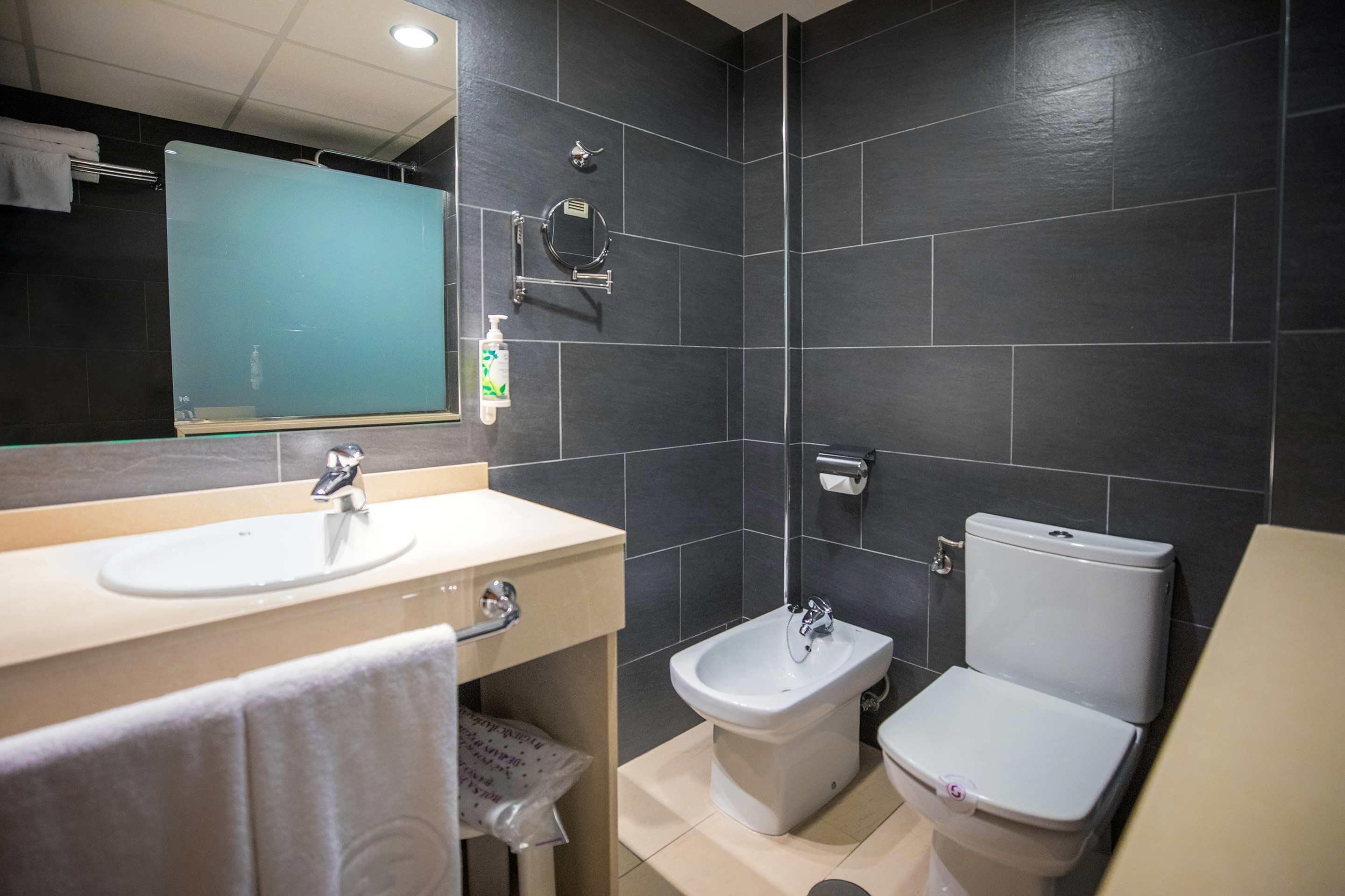 A modern bathroom with a large mirror, two sinks, a bidet, and a toilet.