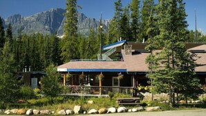 A lodge with a covered porch, a staircase, and a mountain backdrop.