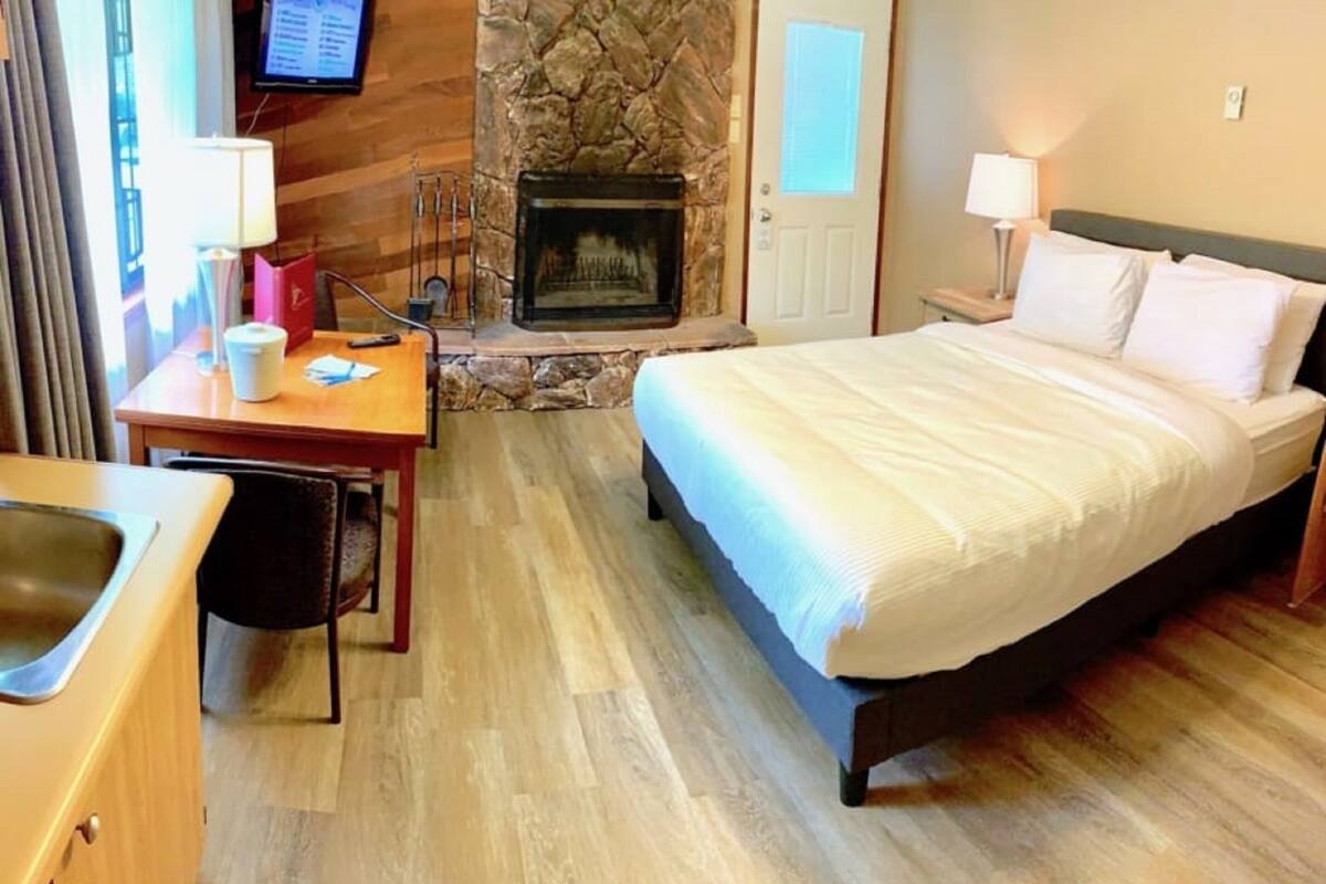 Ein Hotelzimmer mit einem Bett, einem Schreibtisch mit Stuhl, einem Fernseher, einem Kamin aus Stein und einer Tür.