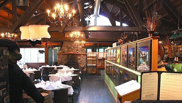A restaurant with wooden beams, chandeliers, and a menu stand. Tables are set with white tablecloths and chairs.