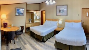 A hotel room with two single beds, a desk with a chair, a vanity with a mirror, and two wall-mounted lamps.
