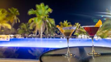 Twee martini glazen op een tafel, met een zwembad en palmbomen op de achtergrond.