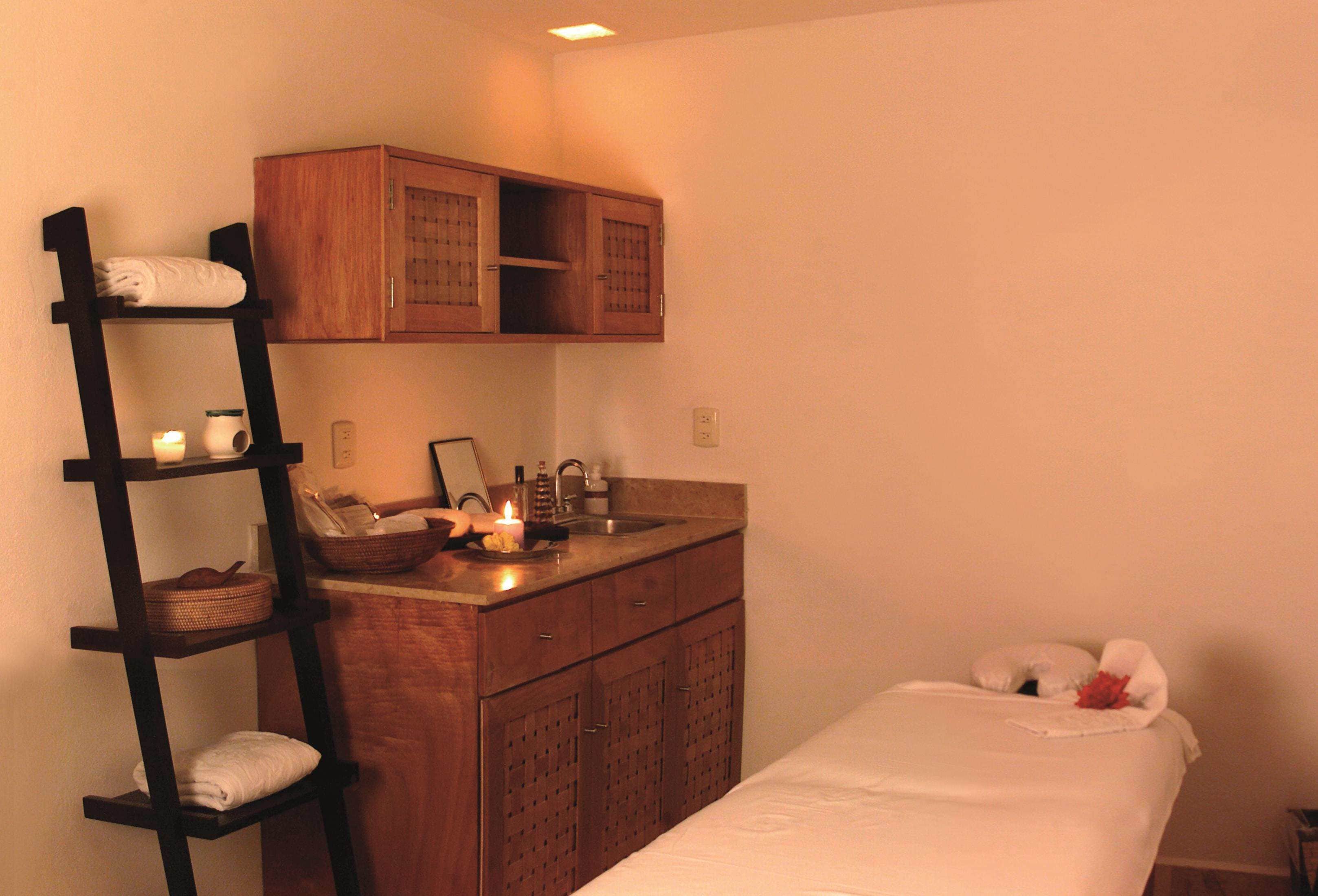 Une salle de bain bien aménagée, avec un meuble-lavabo en bois, une étagère avec des serviettes, un lavabo avec des articles de toilette et un lit recouvert d’une couette blanche.