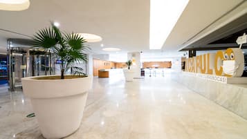 A spacious lobby with a large potted plant, a reception desk, and a sign reading "ACAPULCO".