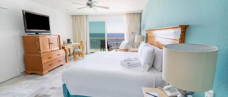 A hotel room with a bed, a television, a desk with a lamp, a phone, and a view of the ocean.