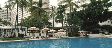 A swimming pool with lounge chairs and umbrellas, surrounded by palm trees and high-rise buildings.