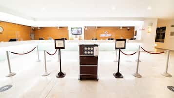 A reception area with a wooden counter, a digital screen, and a check-in kiosk.