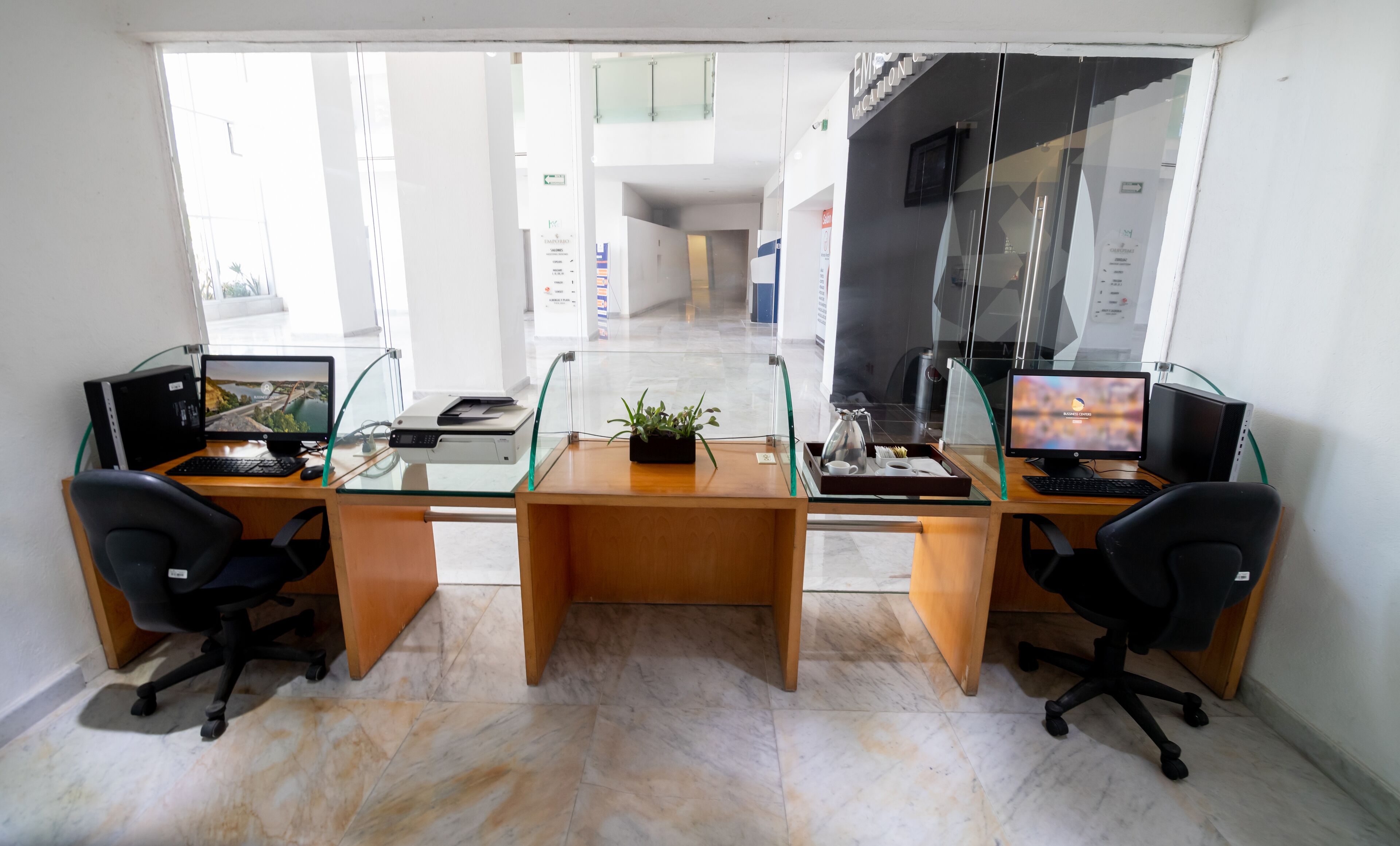 Una oficina moderna con dos escritorios, separadores de vidrio y vistas a una escalera y pasillo.