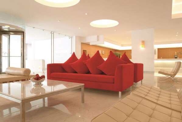 A modern living room with a red sofa, a glass coffee table, and a beige sofa.