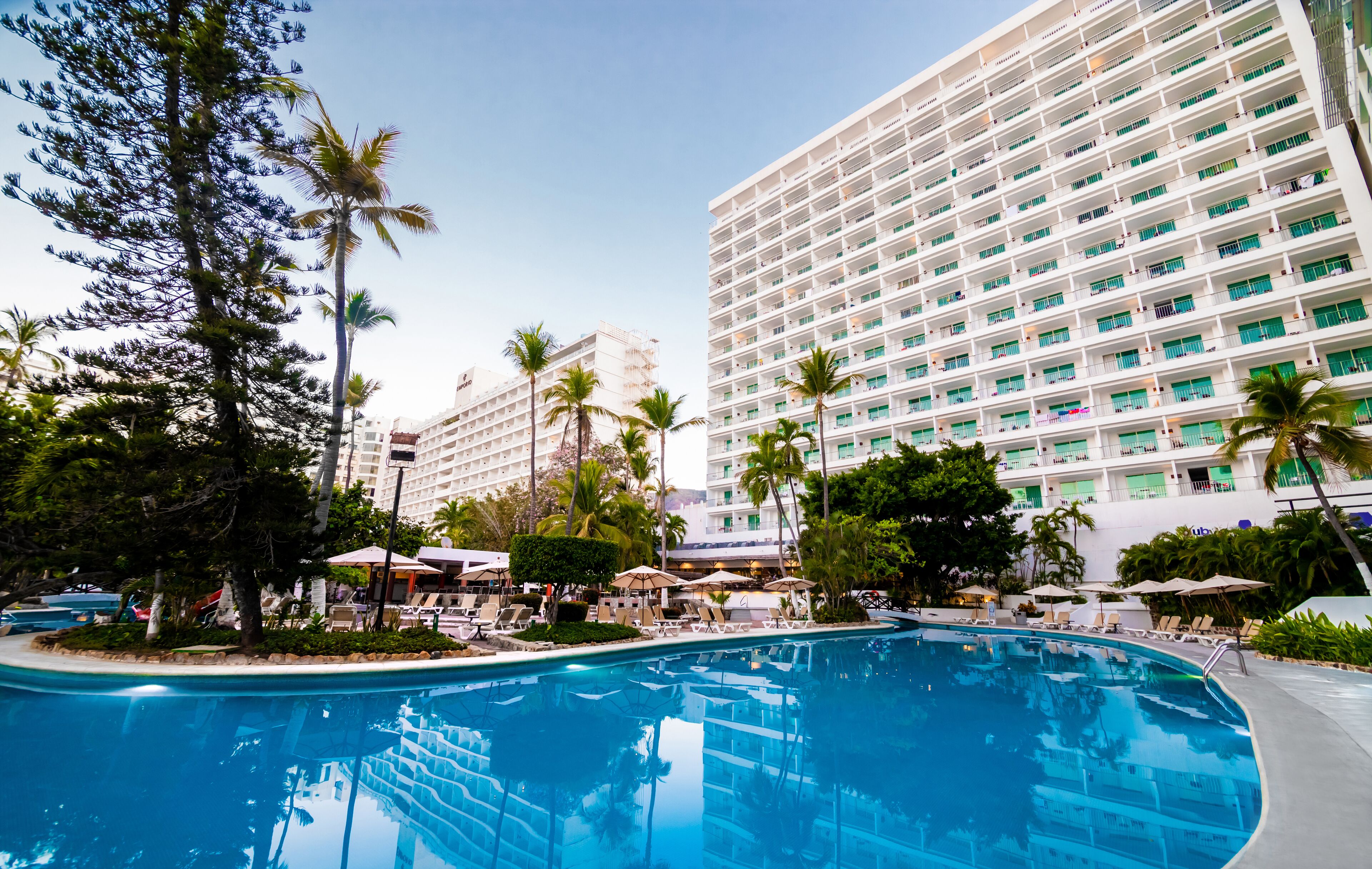 Ein Hotel mit einem großen Pool, umgeben von Palmen und Liegestühlen.