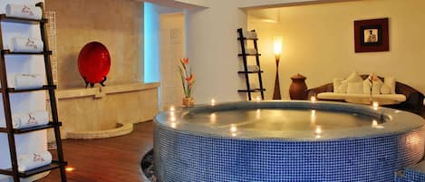 Un cuarto de spa con una bañera de hidromasaje, un estante de madera con toallas, un sofá y un reloj de pared.
