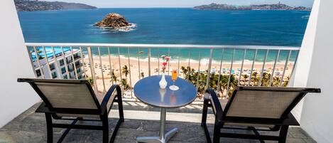 A balcony with two chairs and a table, overlooking a beach and the sea.
