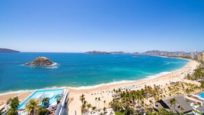 Un complejo turístico frente a la playa con piscina, sombrillas y palmeras.