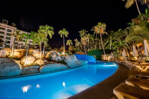 A swimming pool with a water slide, surrounded by palm trees and lounge chairs.