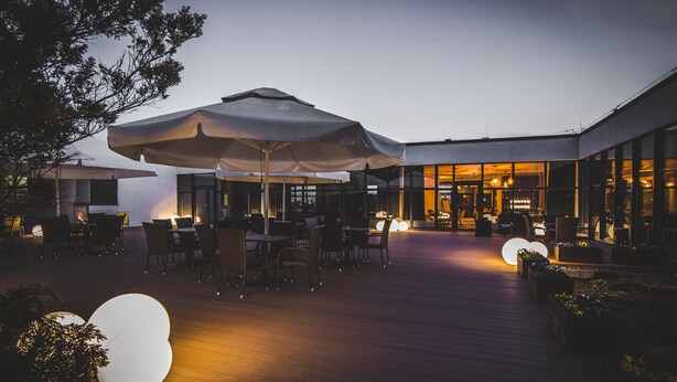 An outdoor dining area with tables and chairs, umbrellas, and a wooden deck. - Mercure Cieszyn (Cieszyn)